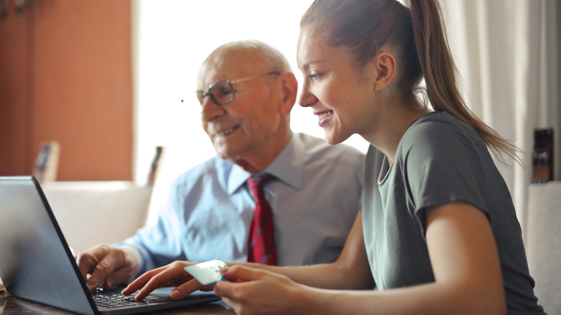 young woman helps elderly men using laptop